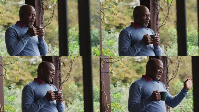 非裔美国高级男子站在阳台上喝咖啡，微笑着挥手