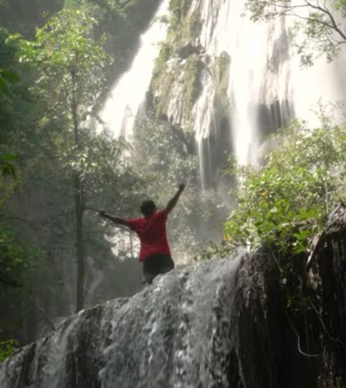穿着红色衬衫的男人在大瀑布和非常沉重的寒冷小溪中幸福和新鲜通过了他的身体