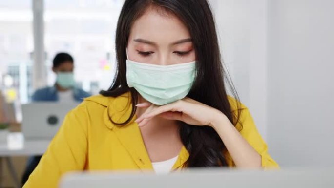 自由职业者亚洲妇女在新的普通家庭办公室使用笔记本电脑努力工作戴口罩。