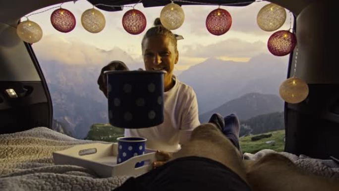 SLO MO女露营者在车上为她的伴侣带来咖啡，并在山上享受早晨