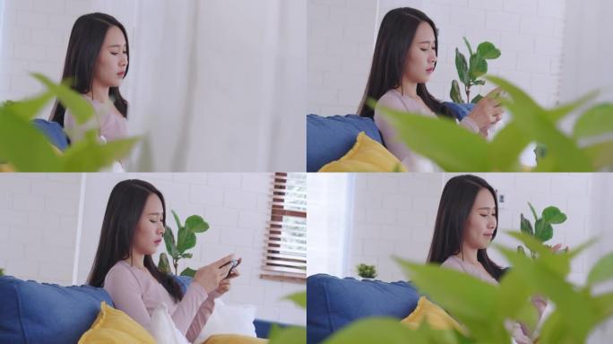 手持和特写镜头迷人的亚洲年轻成年女性在家里的客厅在智能手机上玩在线视频游戏。可爱的年轻女孩喜欢玩游戏