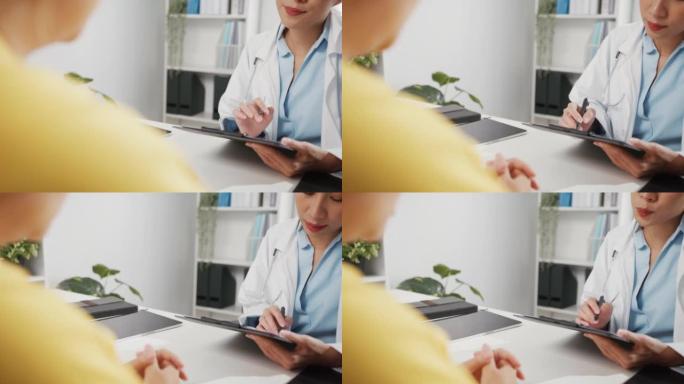 穿着白色医疗制服的年轻亚洲女医生的特写镜头正在用剪贴板与坐在诊所办公室办公桌前的女孩病人分享精彩的新