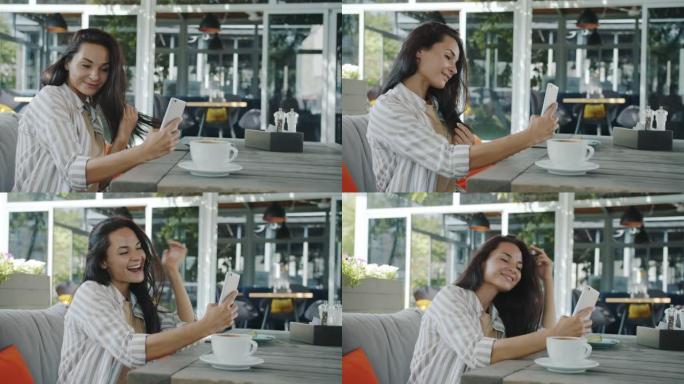 开朗的年轻女士在户外咖啡馆用智能手机相机自拍