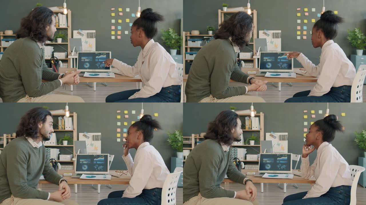 同事混血男子和美国黑人妇女在办公室里聊天和使用笔记本电脑