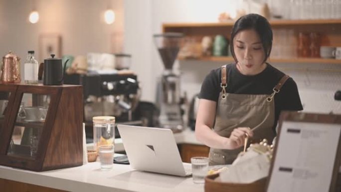 亚洲中国女咖啡师在咖啡店酒吧柜台享用晚餐时使用笔记本电脑
