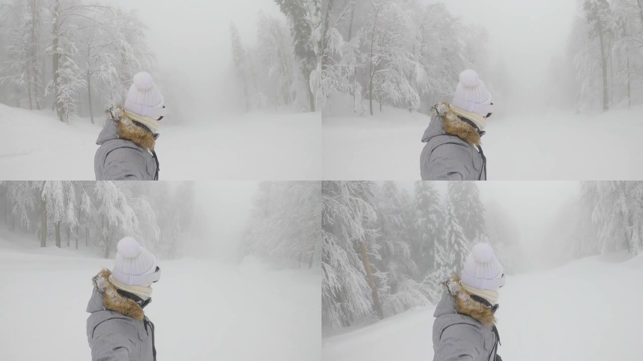 自拍照: 女人在一条经过修饰的斜坡上滑雪板，穿过雾蒙蒙的森林。