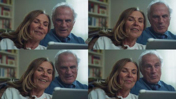 幸福的现代成熟的高级夫妇的电影拍摄坐在家里的客厅沙发上，使用平板电脑进行家庭娱乐。概念: 技术，现代