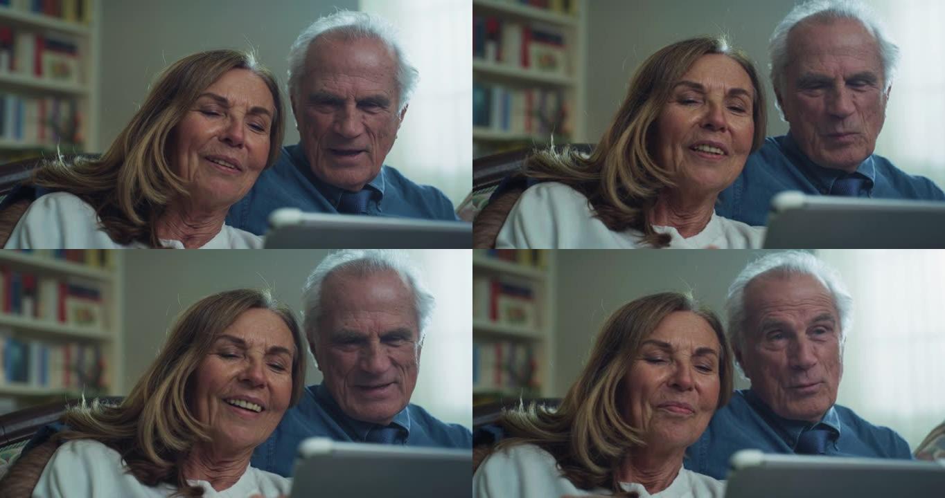 幸福的现代成熟的高级夫妇的电影拍摄坐在家里的客厅沙发上，使用平板电脑进行家庭娱乐。概念: 技术，现代
