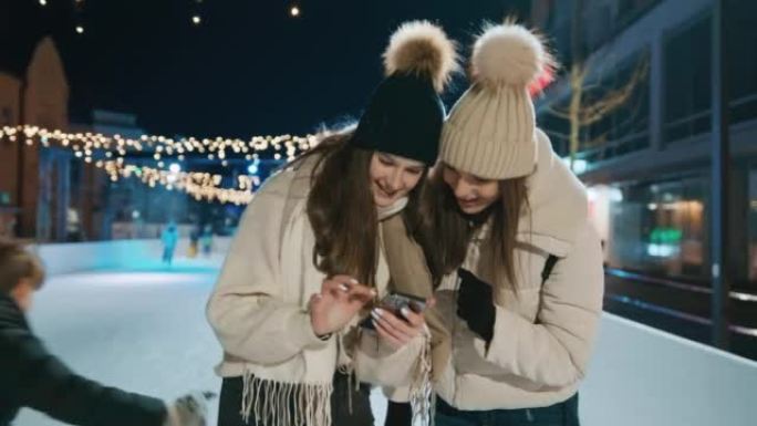 两名年轻妇女在圣诞节期间在溜冰场上使用手机