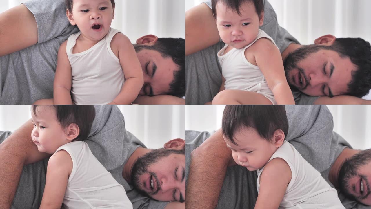 疲惫的千禧一代亚洲父亲睡在床上，男婴打哈欠捂着嘴。