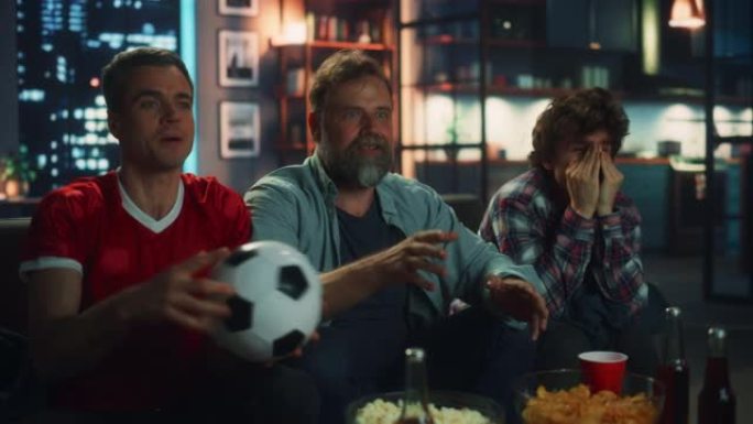 晚上在家: 三个快乐的足球迷坐在电视上的沙发上观看比赛，当运动队赢得冠军时庆祝胜利。一群朋友为最喜欢