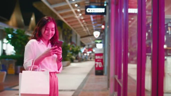 年轻的亚洲妇女使用电话并看着商店橱窗商店