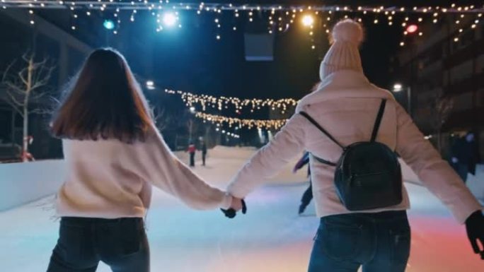 两名年轻女子手牵手在溜冰场上滑冰的后视图