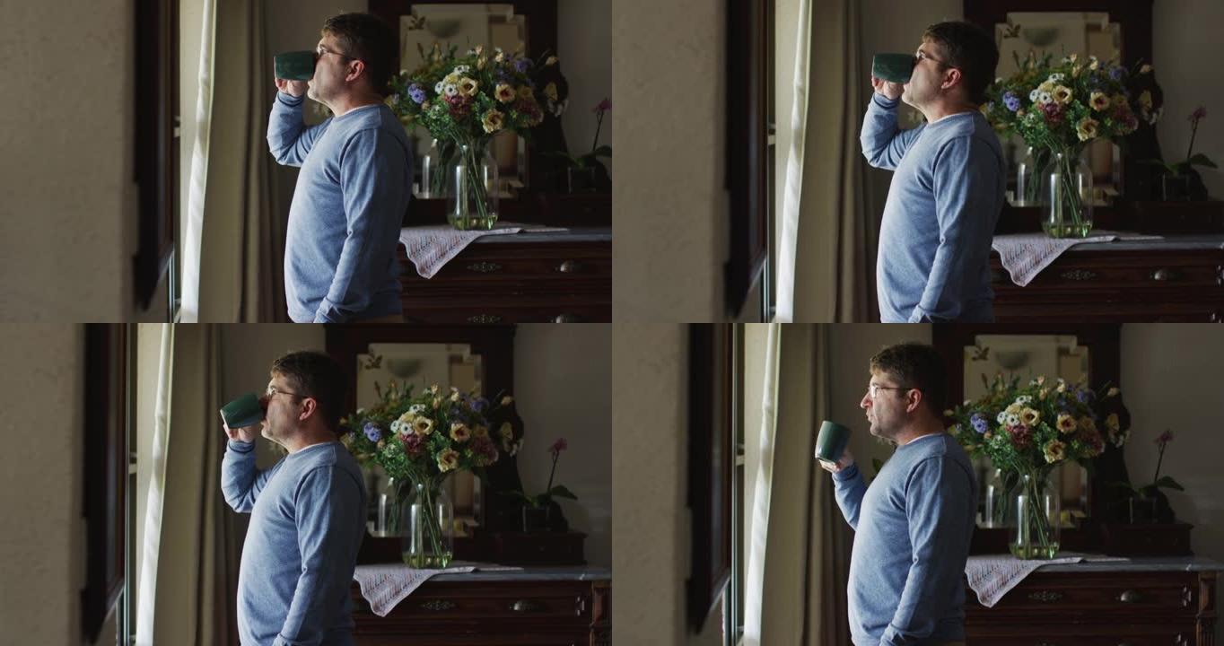 体贴的白人男子站在窗前在家喝咖啡