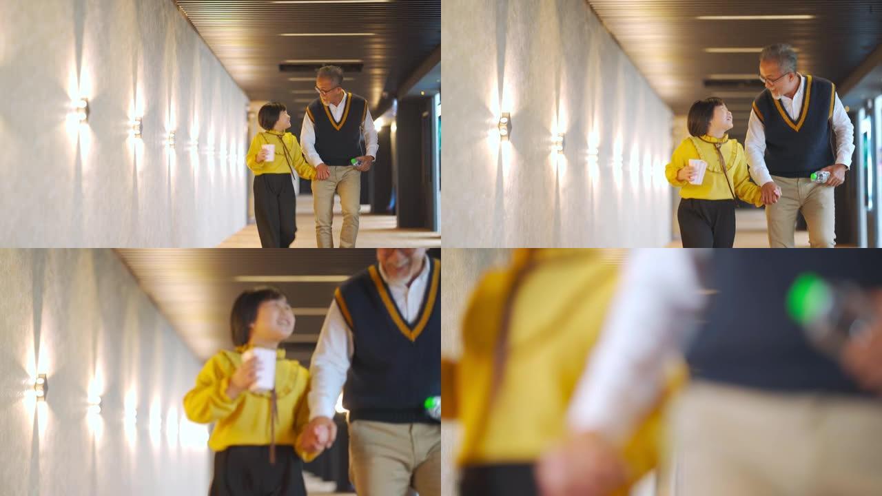 亚洲华裔高级男子祖父在周末牵着孙女的手走在走廊上看电影