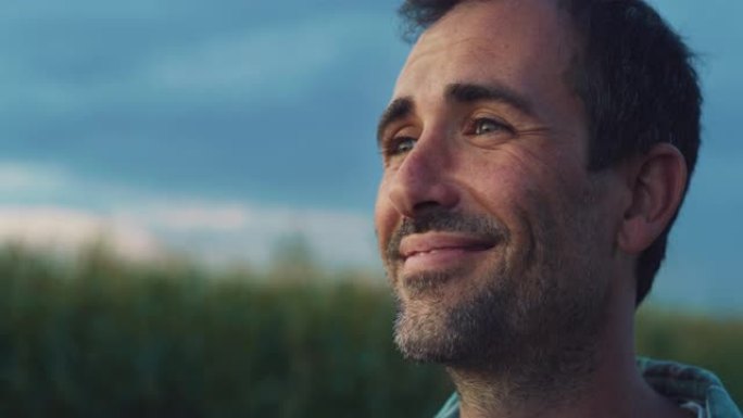 一个男人微笑着在一片绿色的玉米田里环顾四周。英俊的中年男性农民享受大自然，感谢好天气，对他的庄稼和生