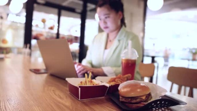 女商人在笔记本电脑上工作，在餐厅餐桌上吃快餐