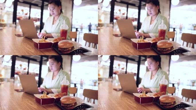 女商人在笔记本电脑上工作，在餐厅餐桌上吃快餐