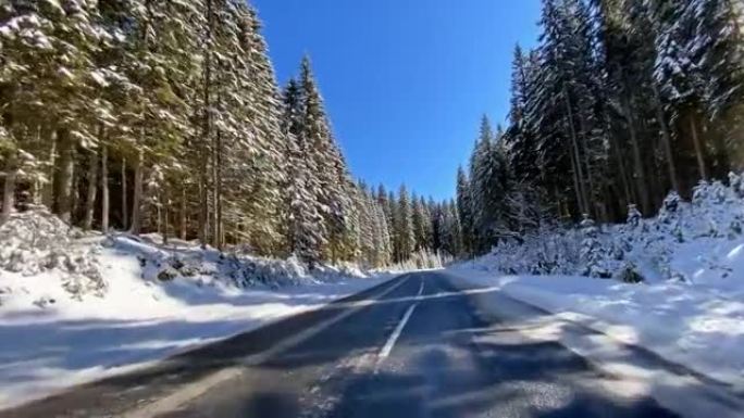 在阳光明媚的日子里，冬天在积雪覆盖的森林的空旷道路上行驶