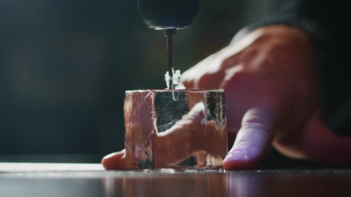 专业调酒师的特写镜头正在切割专业水晶持久冰块，为酒吧或迪斯科俱乐部的顾客准备精英酒精鸡尾酒。