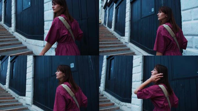 年轻快乐迷人的黑发白人旅游妇女，穿着紫色连衣裙，沿着蓝色墙壁的老城楼梯行走。