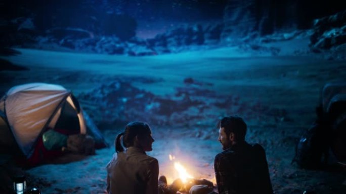 快乐的情侣帐篷在峡谷里露营，坐在篝火旁看着夜空，银河里满是明亮的星星。两个恋爱中的旅行者在浪漫的假期