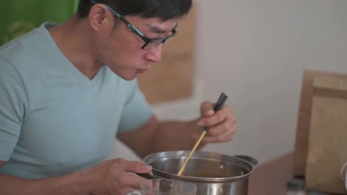亚洲中国男子享受汤面与锅和筷子美味