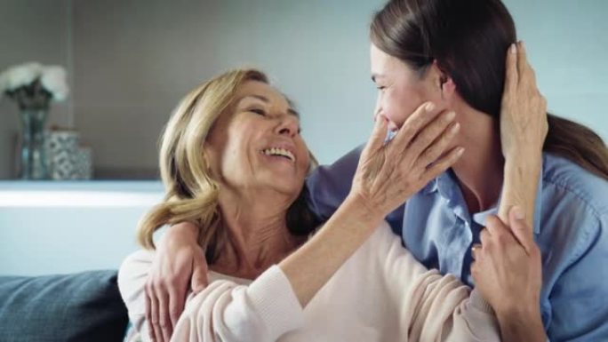 快乐孙女的电影镜头正在给祖母以情感的拥抱，以示爱与尊重，同时坐在家里的沙发上。概念: 生活，祖父母，