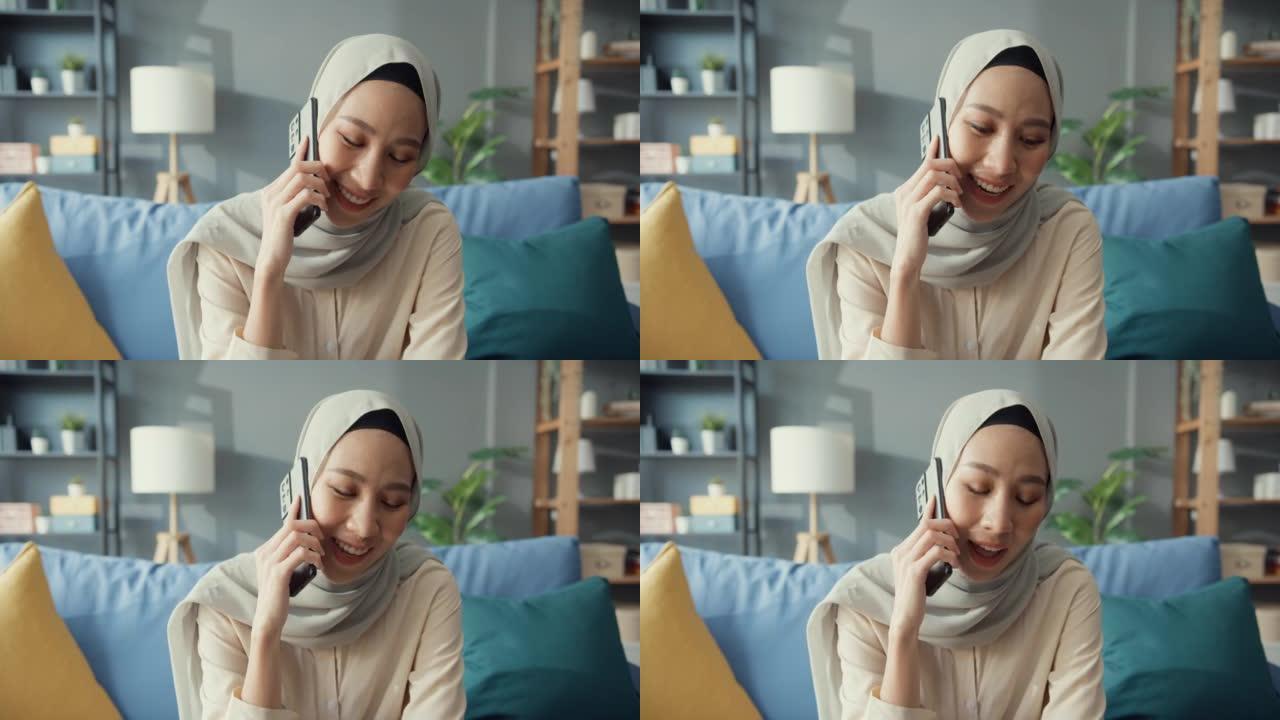 迷人的年轻亚洲穆斯林美女戴着头巾，在家里舒适的客厅与朋友和家人随意打电话。女孩伊斯兰社会距离检疫生活