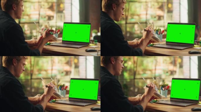 男性设计师在带有绿屏模拟色度键的笔记本电脑前的鞋子上绘画。十几岁的自由职业者在他的工作室设计独特的鞋