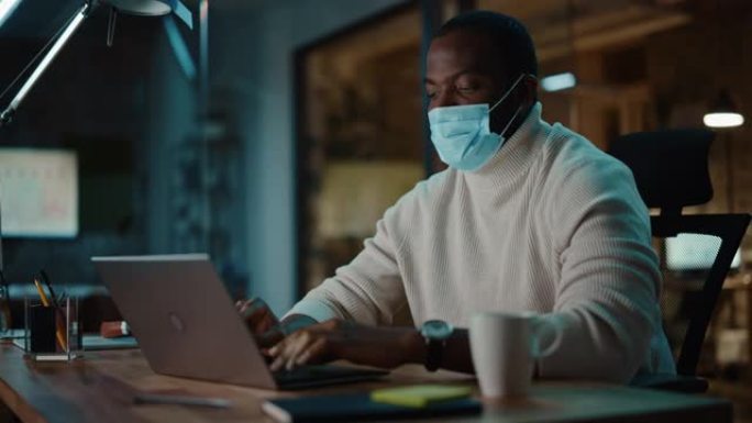 黑人非裔美国人在创意机构的笔记本电脑上进行在线对话时戴着口罩。冠状病毒大流行期间商务办公中的社会限制