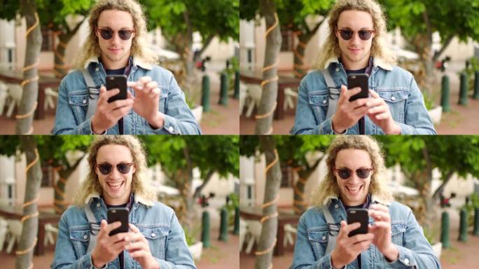 年轻的快乐男子笑着，站在城市里用电话在线阅读短信。一位酷炫，时尚，时尚的男性使用社交媒体与朋友聊天并