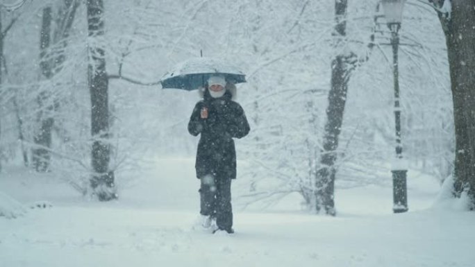 慢动作: 暴风雪期间，穿着厚厚的冬衣的年轻女子在公园里走来走去
