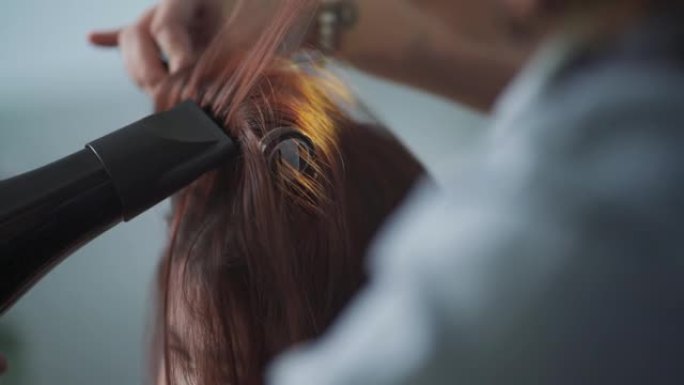 后视慢动作亚洲中国女性发型师吹风为她的顾客梳理湿长发美发沙龙