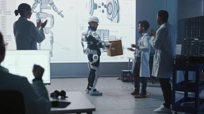 在开发实验室中: 工程师和科学家看着机器人外骨骼演示，有人举起沉重的Carboard Box，人们在