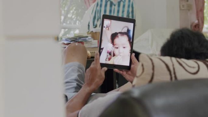4k分辨率手持射击亚洲高级妇女手持平板电脑设备，并通过视频通话或视频会议技术与孙女交谈，同时在冠状病
