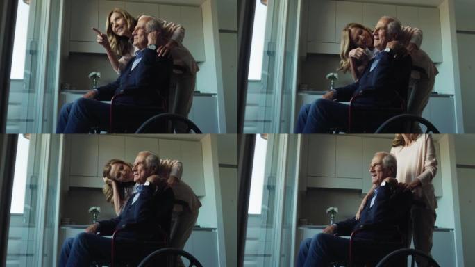 微笑的成熟妻子拥抱轮椅上的残疾丈夫的电影镜头，是在家里透过窗户看时永远永恒的爱的标志。生活观念，家庭