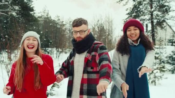 有趣的快乐宁静的多民族年轻朋友在美丽的白雪皑皑的冬季森林慢动作中穿着暖和的衣服一起跳舞。