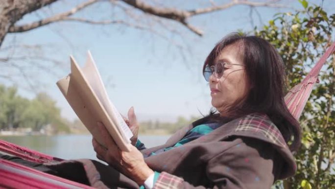 高级妇女在公园的吊床上放松阅读书籍