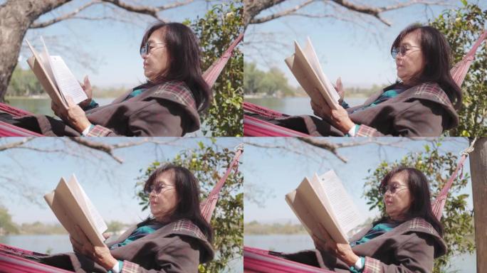 高级妇女在公园的吊床上放松阅读书籍