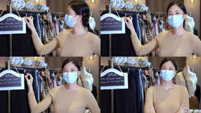 亚洲妇女在服装店靠卖招牌，戴着口罩