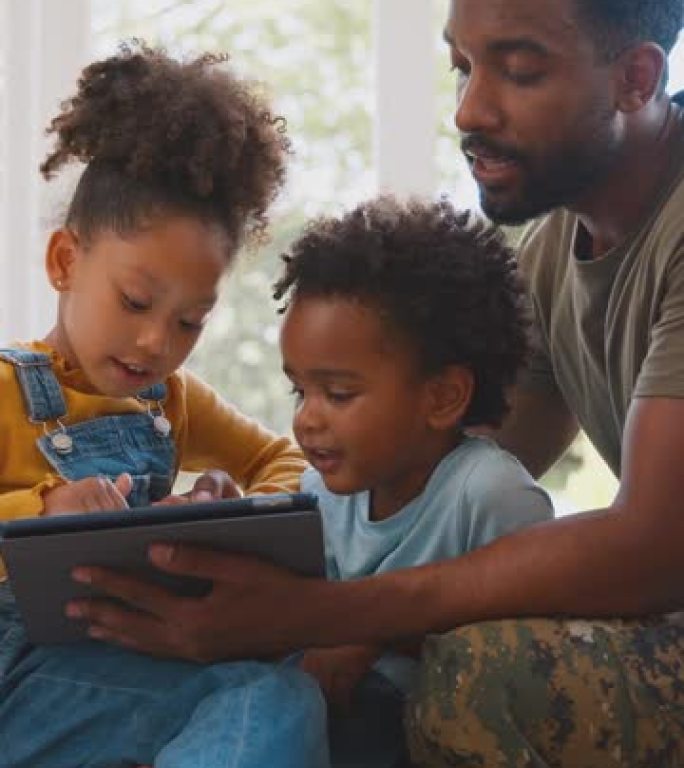 军中父亲穿着制服坐在沙发上，与孩子们一起玩游戏或将电影传输到数码平板电脑上——用慢动作拍摄