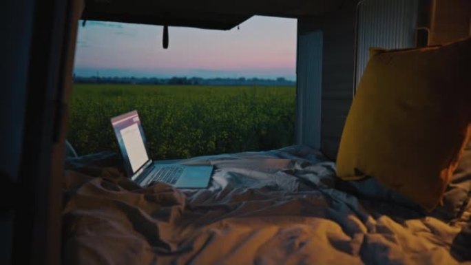 DL笔记本电脑在露营车的床上，黄昏时停在油菜籽田中间