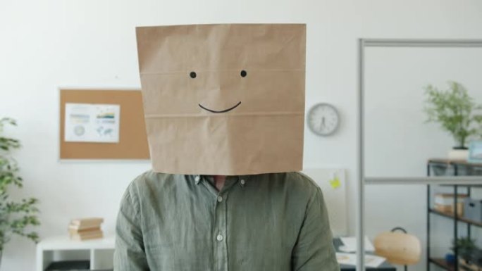 男员工穿着纸袋的肖像，微笑表情符号站在办公室看着相机