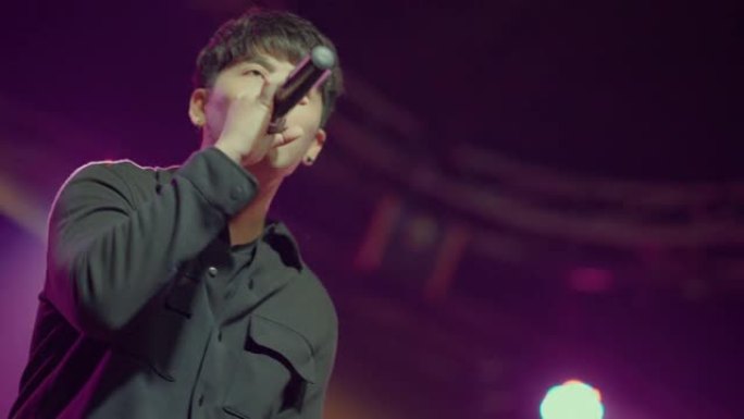 年轻的亚洲摇滚歌手在空旷的舞台和多色的聚光灯下唱歌。