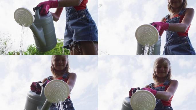 微笑的高加索女孩在花园用喷壶浇灌植物中的低角度视图