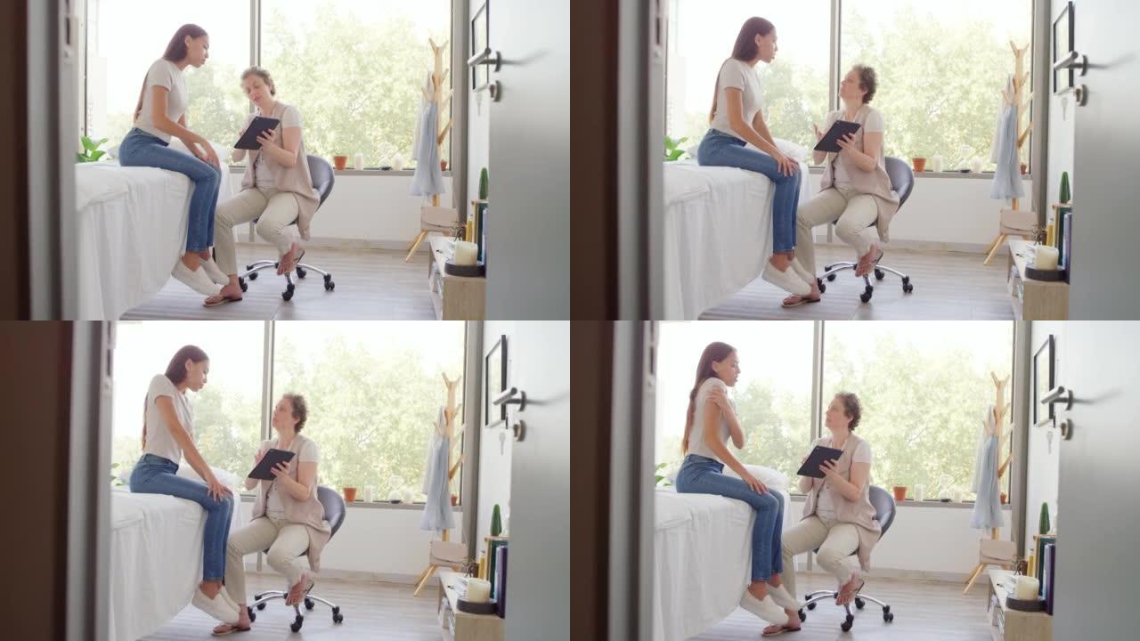 女医生使用平板电脑，并向女性提供有关肩部疼痛的医疗建议。脊医显示病人扫描结果。高加索按摩治疗师与坐在