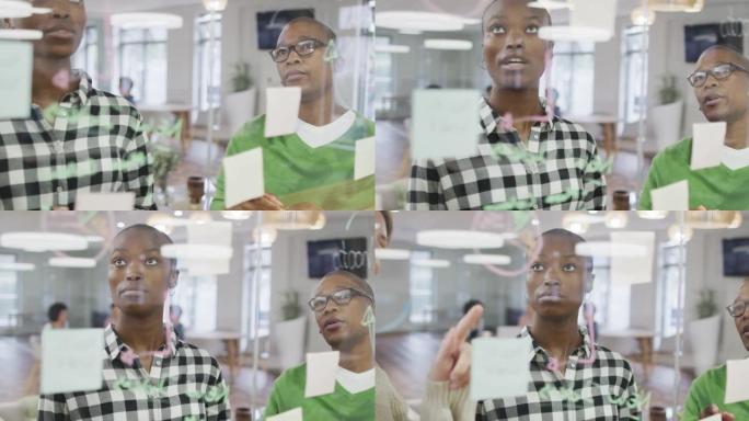 非裔美国女性商业同事在玻璃墙上讨论备忘录