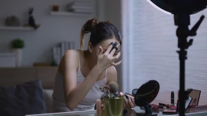 年轻的亚洲女性美容博主拍摄日常化妆常规教程使用三脚架上的手机环形灯
