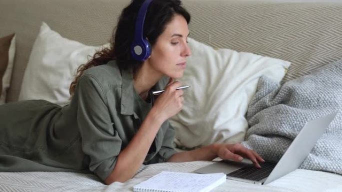 女人躺在室内戴耳机听音频课程记信息